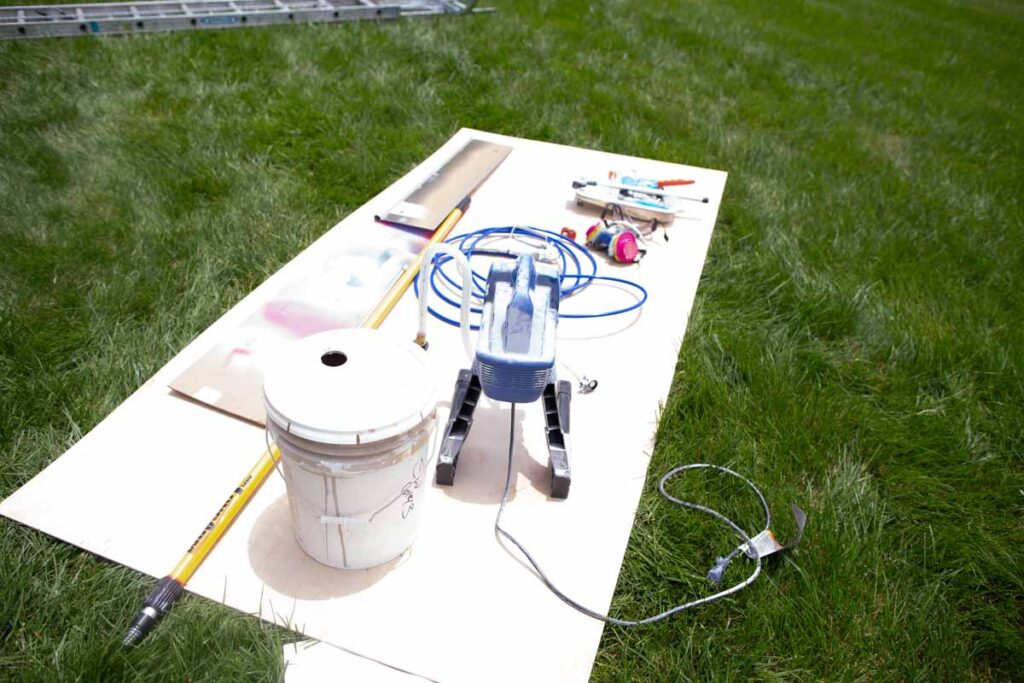 preparation and tools for spraying a house exterior with supplies laid out on the grass