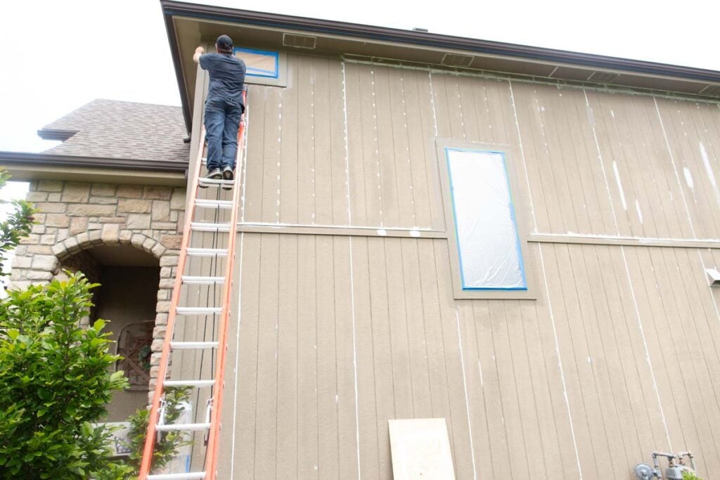 man on large ladder painting the top of a house