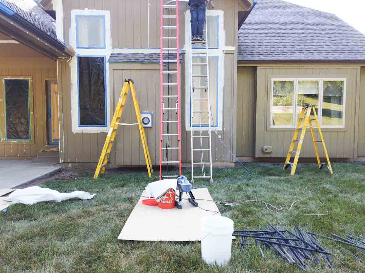 ladders against house while man painting with a a spray paint gun